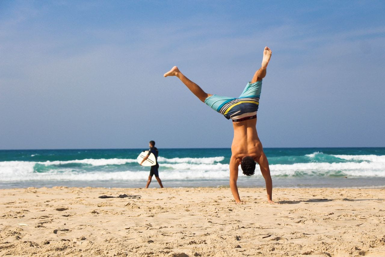 physically fit man doing a handstand on the beach