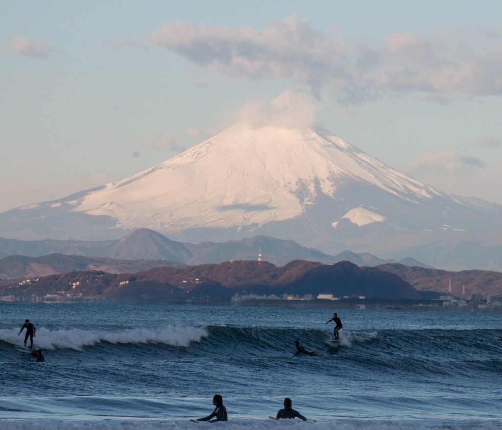 Surfers ride waves at Shonan surf spot in Japan with mountain in background