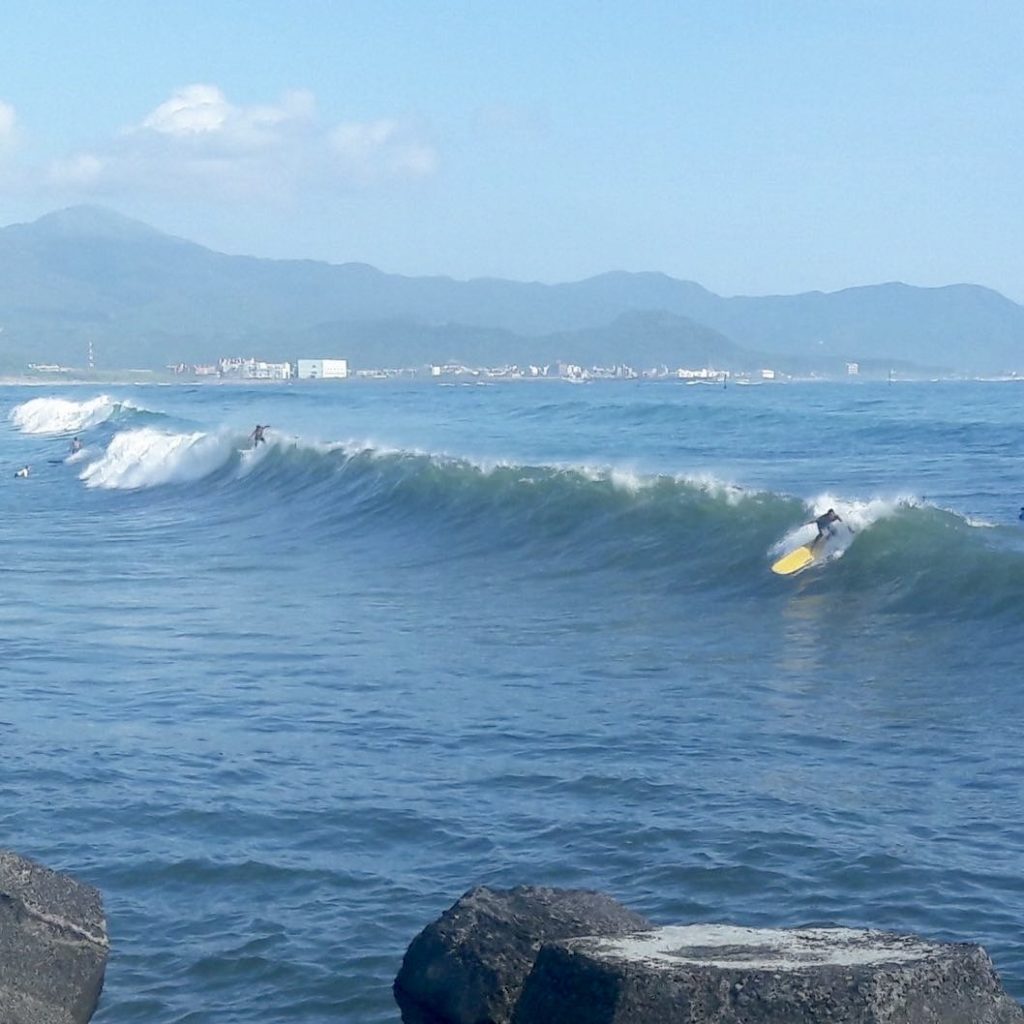 Surfers ride waves with mountains in the background at Furlong Beach in Taiwan