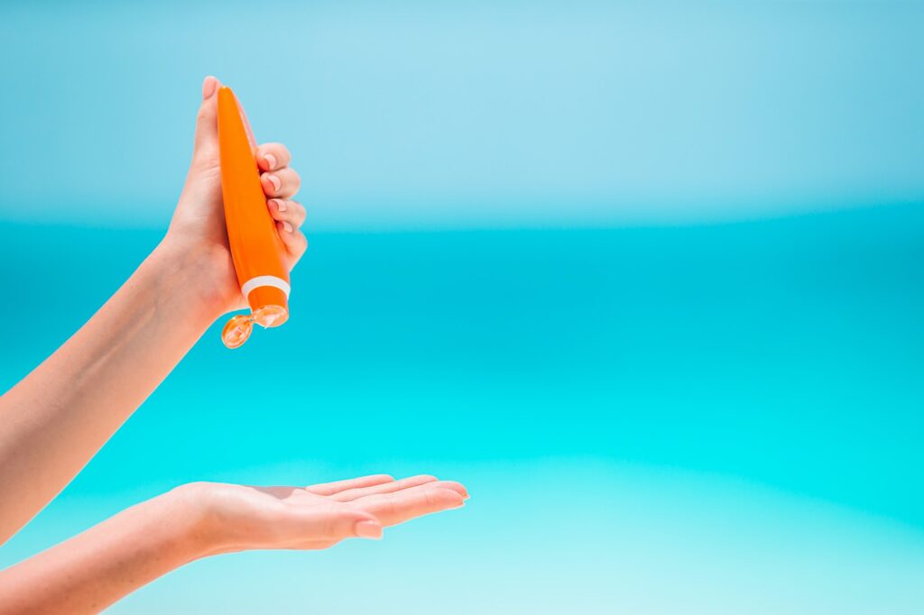 Beautiful young woman holding a suncream lying on tropical beach
